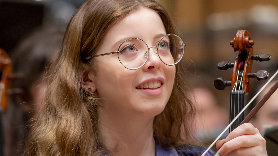 An RCM student holding their violin and looking up in rehearsals